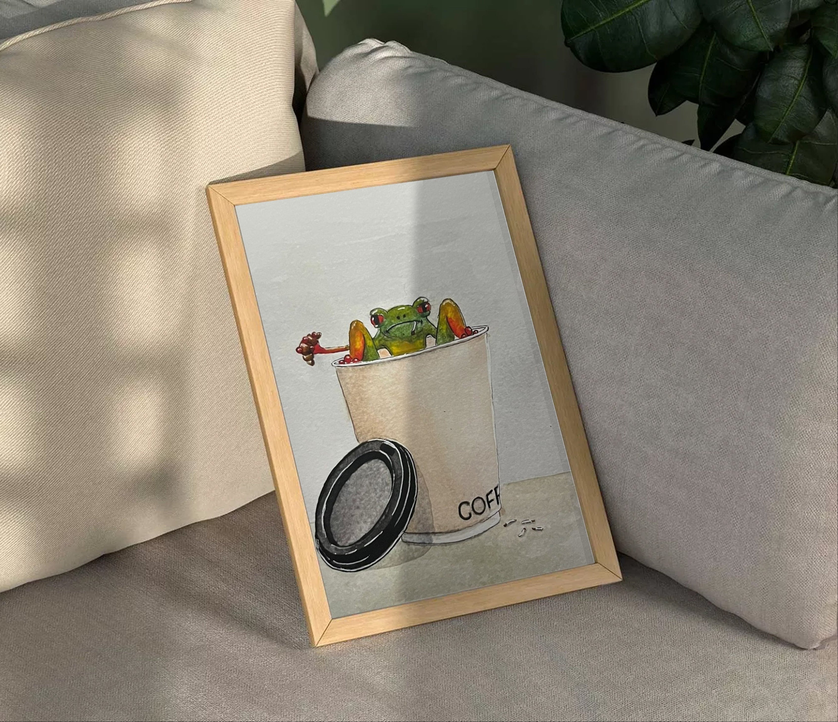 Framed artwork of a coffee cup with colorful creatures on a couch